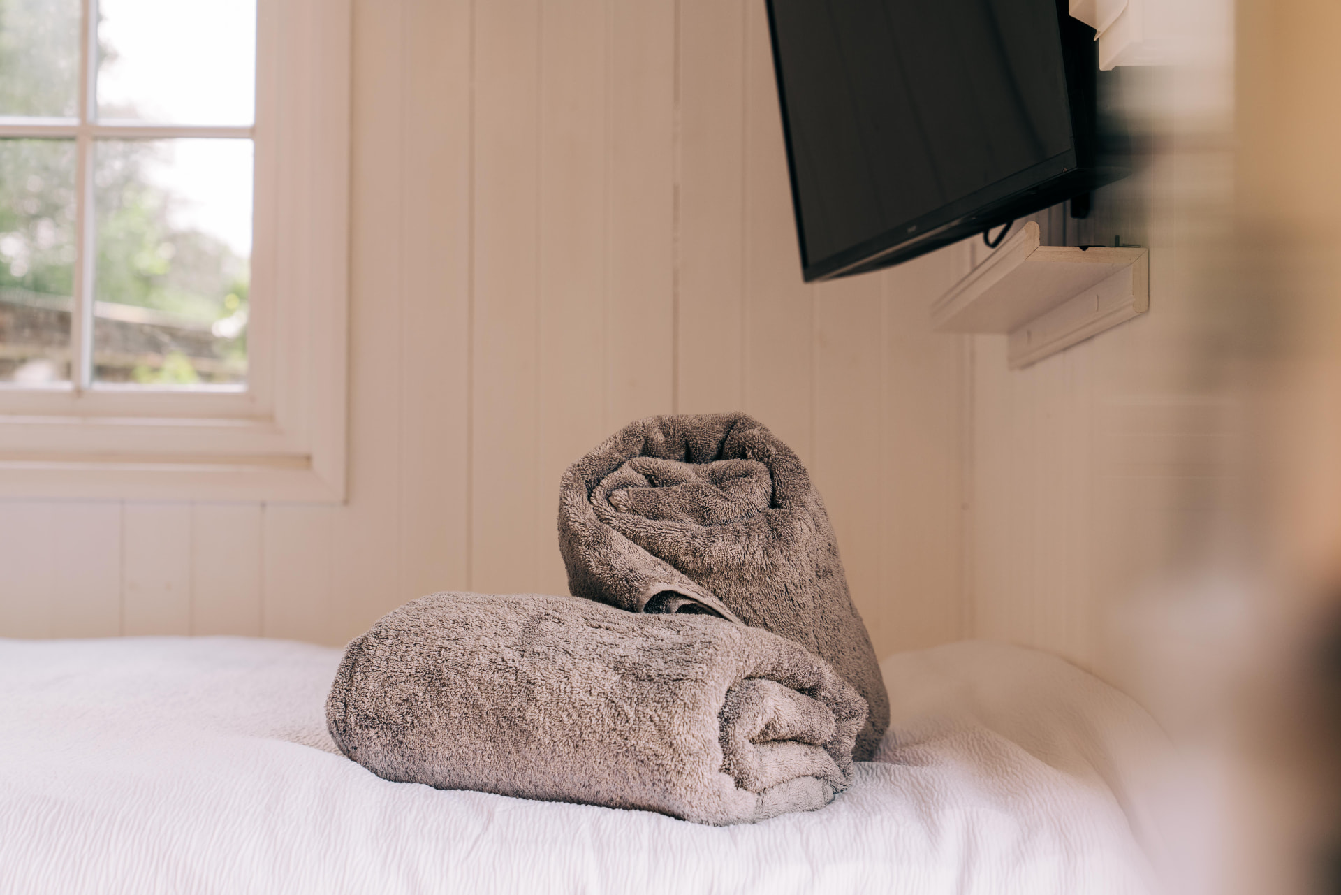 Rolled grey towels on the freshly made bed